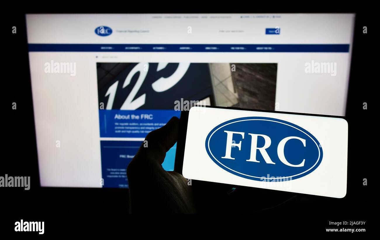Person, die das Mobiltelefon mit dem Logo des Financial Reporting Council (FRC) der Regulierungsbehörde auf dem Bildschirm vor der Webseite hält. Konzentrieren Sie sich auf die Telefonanzeige. Stockfoto