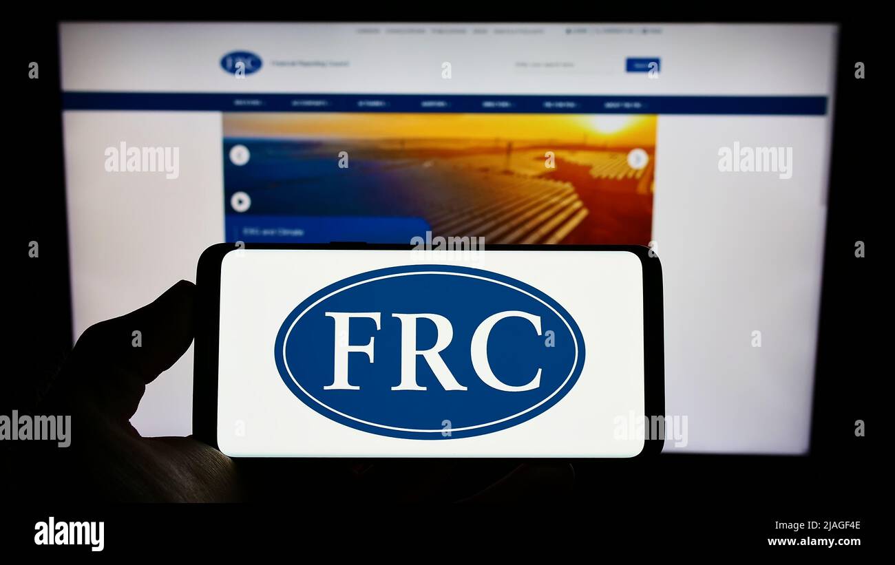 Person, die Mobiltelefon mit dem Logo der britischen Regulierungsbehörde Financial Reporting Council (FRC) auf dem Bildschirm vor der Webseite hält. Konzentrieren Sie sich auf die Telefonanzeige. Stockfoto