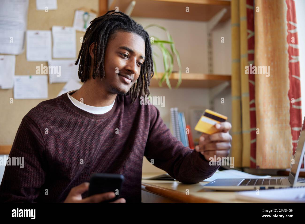 Männlicher Universitäts- oder Hochschulstudent mit Kreditkarte, die Online-Kauf am Schreibtisch im Zimmer macht Stockfoto