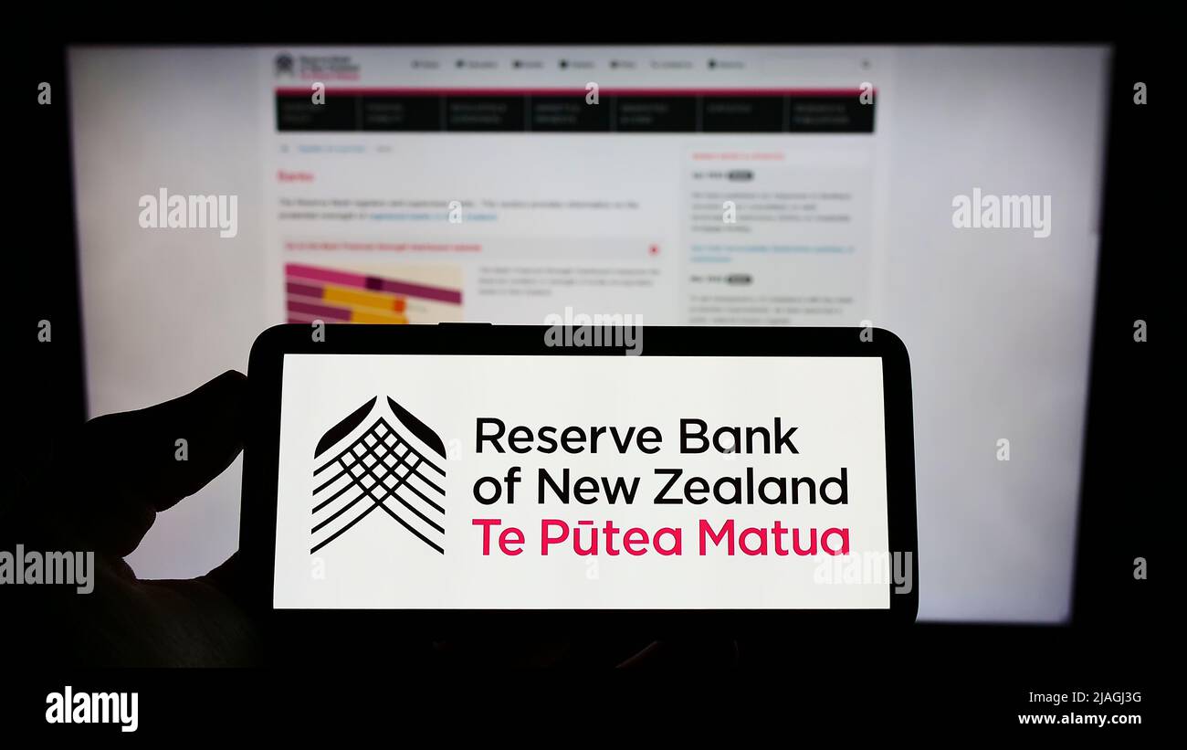 Person mit Mobiltelefon und Logo der Zentralbank Reserve Bank of New Zealand (RBNZ) auf dem Bildschirm vor der Webseite. Konzentrieren Sie sich auf die Telefonanzeige. Stockfoto