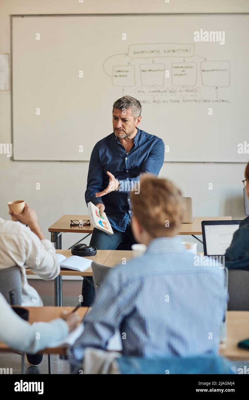 Männlicher Lehrer gestikuliert, während Schüler Unterricht Klassenzimmer Stockfoto