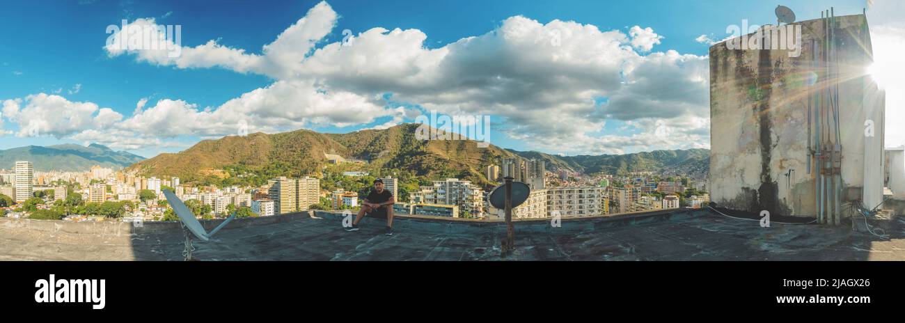 Der junge Mann sitzt auf einem Dach und schaut in die Stadt Caracas, Venezuela. Stockfoto