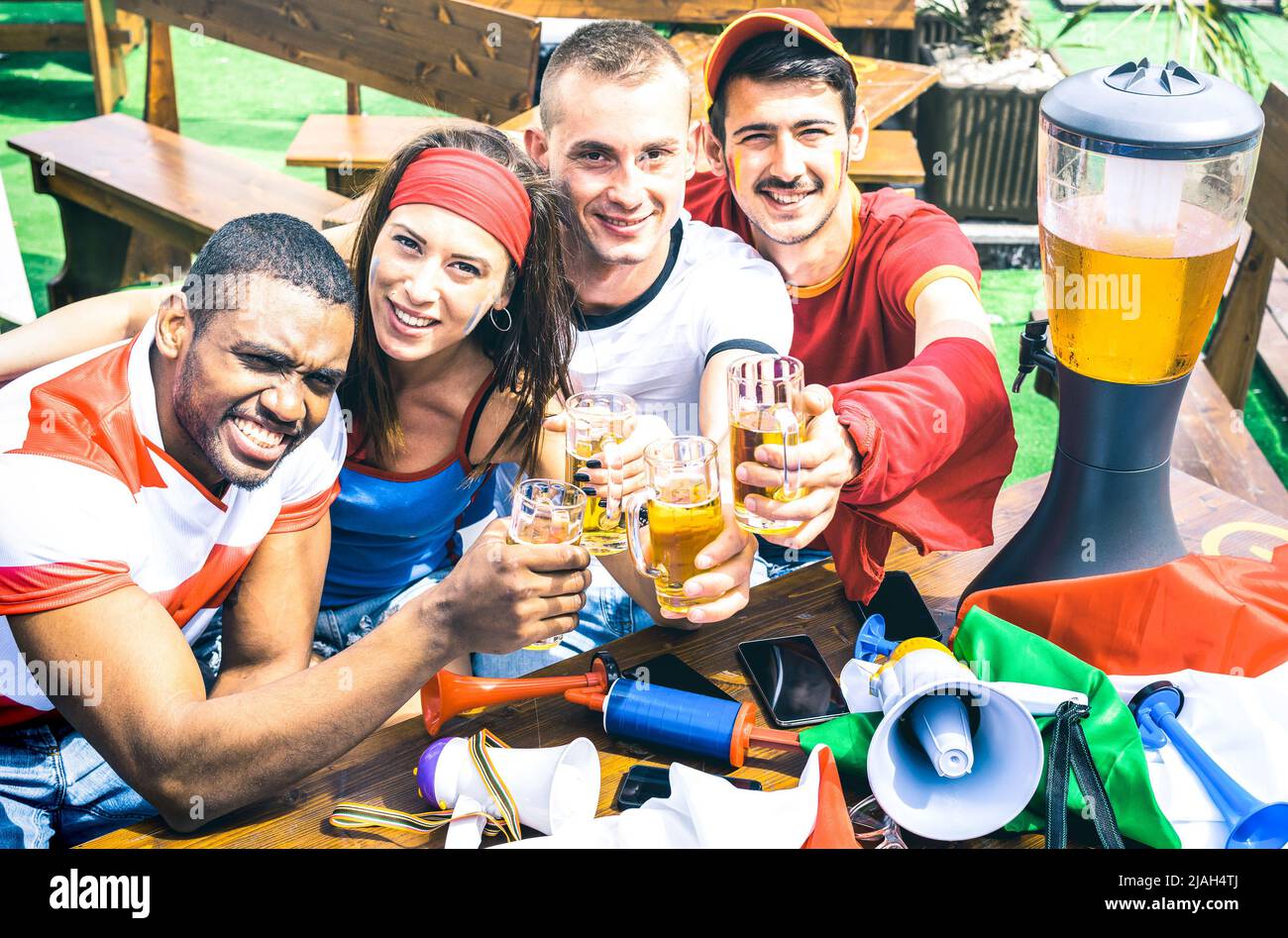 Junge Fußballfans, die Bier beim Fußballspiel im fernsehen toasten - Freunde Leute mit bunten T-Shirts und Fahnen, die Spaß haben - Sportchamps Stockfoto