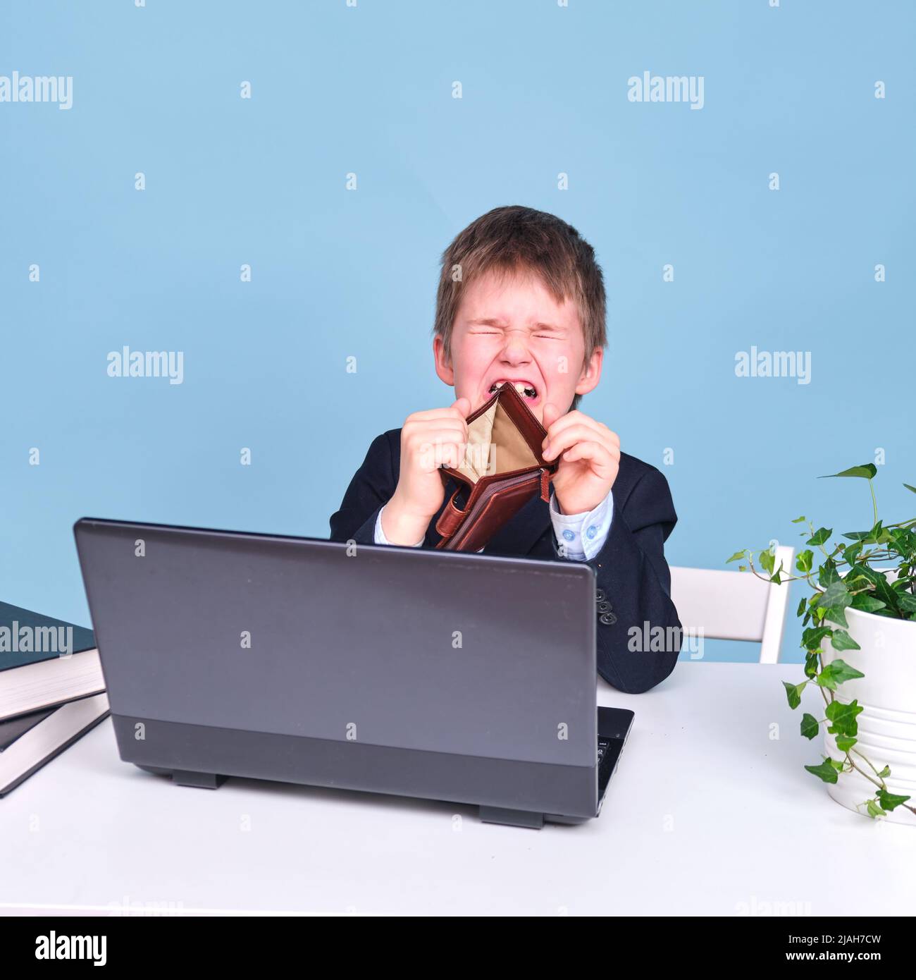 Ein Junge in einem Schulanzug mit einer leeren Brieftasche, kopieren Sie Platz auf einem blauen Studiohintergrund Stockfoto