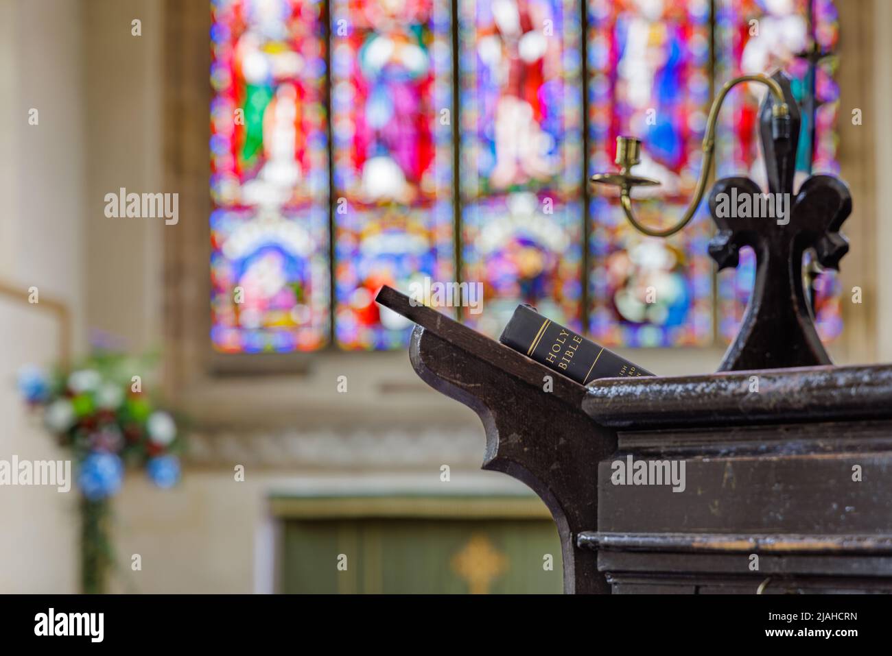 Crick, Northamptonshire, UK, Mai 30. 2022: Vor einem Buntglasfenster ruht ein Buch mit der Heiligen Bibel auf dem Rücken auf einem Rednerpult in einer Kirche. Stockfoto