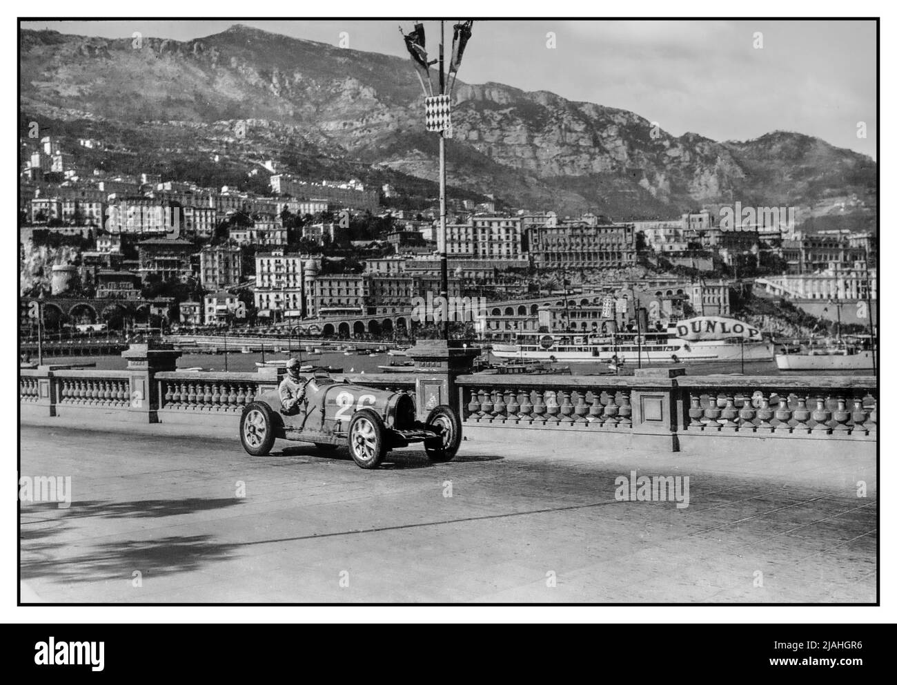 Der Grand Prix von Monaco 1931 mit Achille Varzi fuhr einen Bugatti Nummer 26 mit dem Hafen von Monaco dahinter. Der Grand Prix von Monaco 1931 war ein Grand Prix, der am 19. April 1931 auf dem Circuit de Monaco ausgetragen wurde. Mit 16 Bugattis auf einem Feld von 23 Autos war das Rennen fast ein Single-Make-Rennen. Zu den 16 gehörten vier Fabrikteams vom Typ 51, die vom monegassischen Louis Chiron, dem Italiener Achille Varzi und dem Franzosen Albert Divo und Guy Bouriat angetrieben wurden. Stockfoto