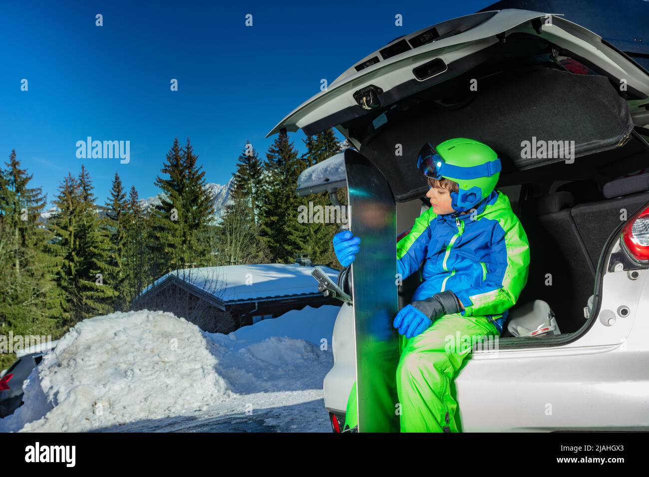 Boy mit Snowboard in Helm, Maske sitzen auf dem Parkplatz Stockfoto