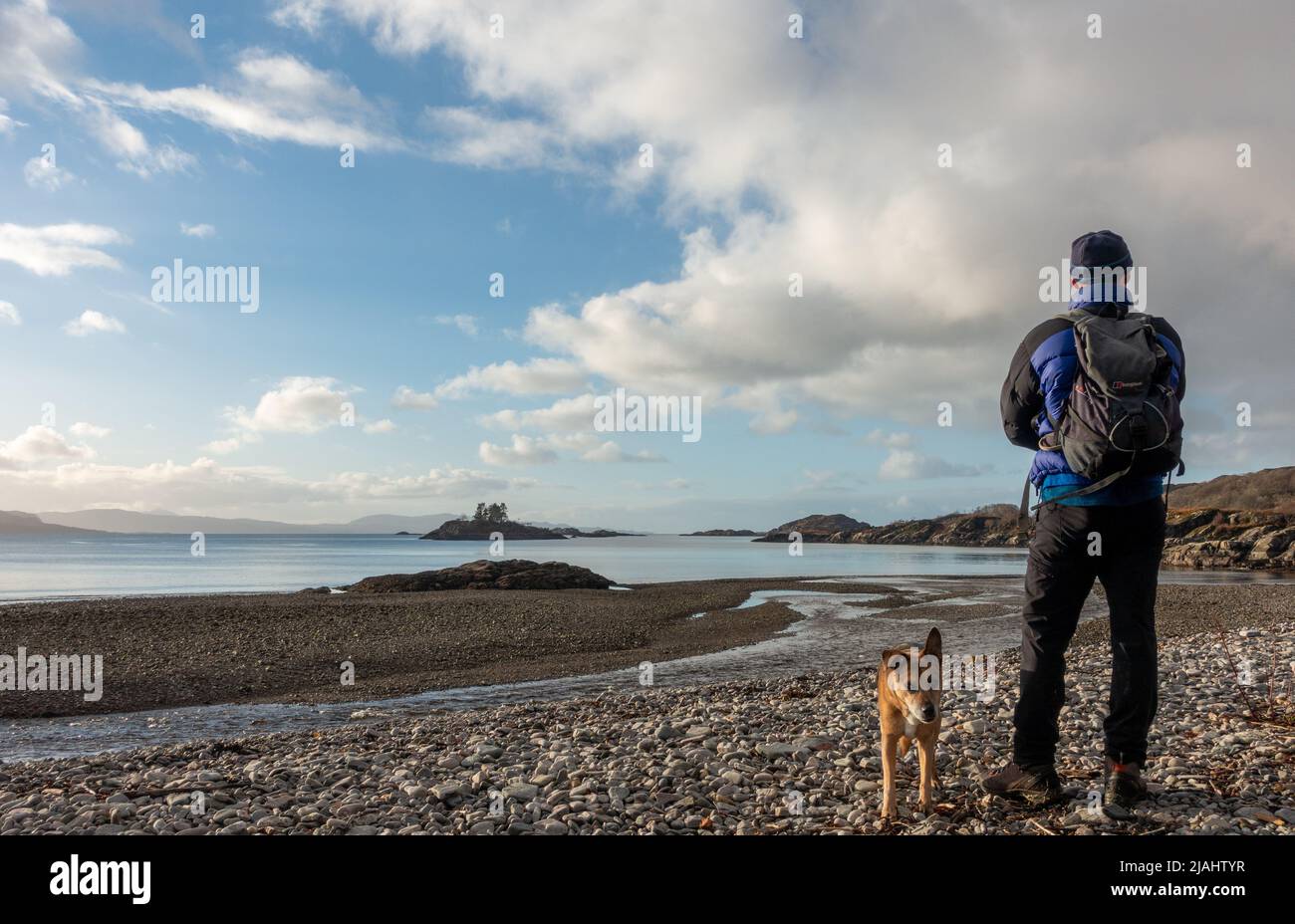 Schottische Landschaft - Person mit Hund bewundern die Aussicht auf die atemberaubende wilde Lage von Druimindarroch und Borrodale Beach im Winter, in der Nähe von Arisaig, SC Stockfoto