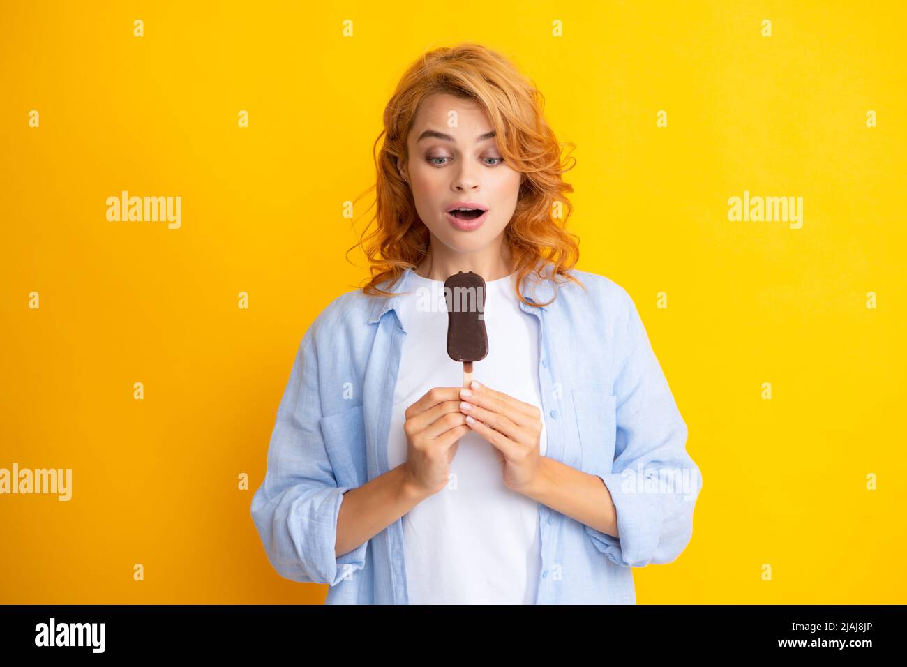 Foto von jungen Frau isst leckeres Eis, genießt gefrorene Dessert, in legerer Kleidung gekleidet, isoliert auf gelbem Hintergrund. Stockfoto