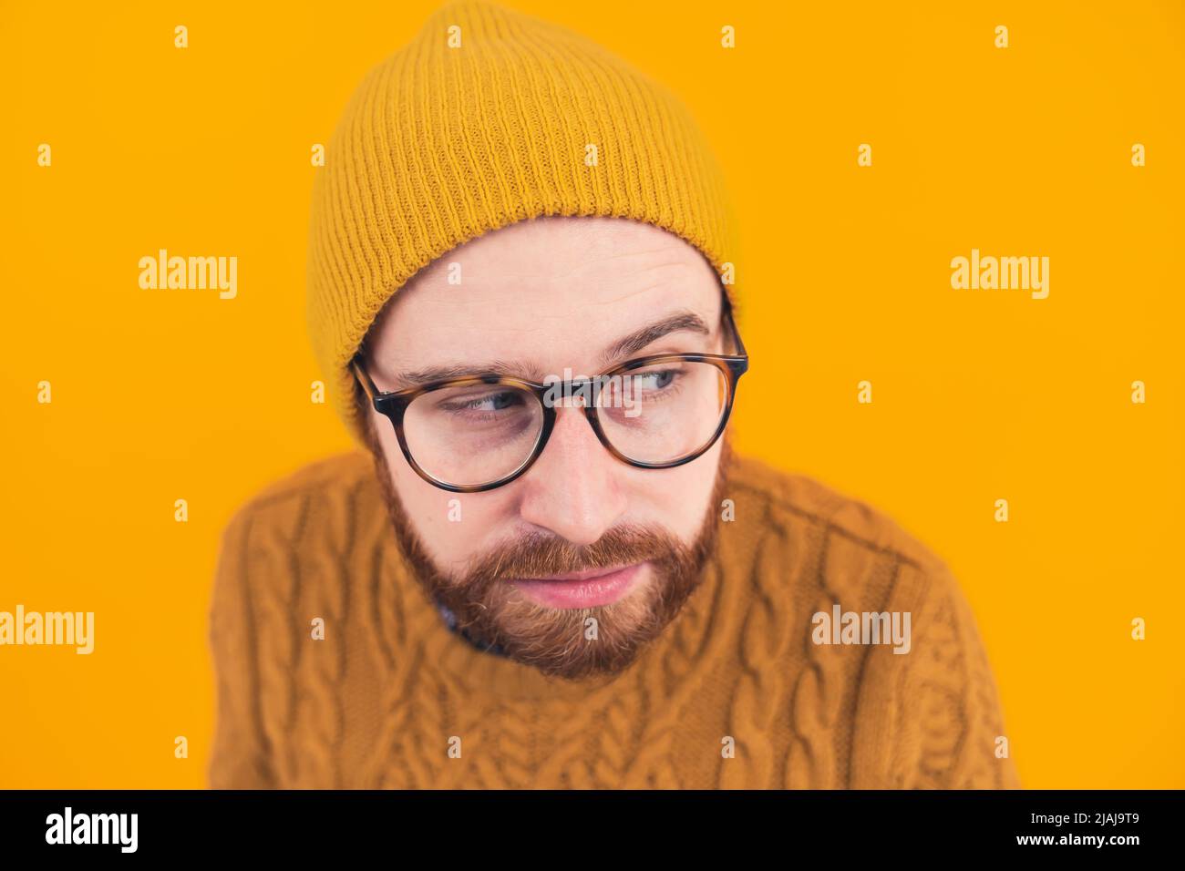 Studioportrait eines lustigen, verdächtigen bärtigen kaukasischen Mannes in einer Mütze und einer dunklen Brille, die seine Augenbraue aufsteigt. Gelber Hintergrund. Hochwertige Fotos Stockfoto