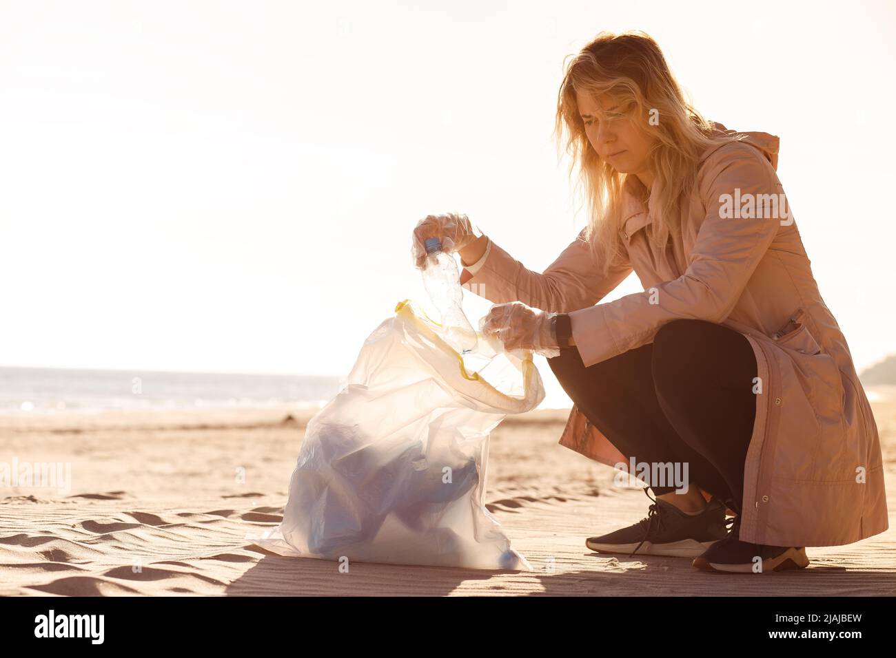 Eine Freiwillige sitzt am Strand und hilft dabei, Meeresmüll aus Plastik zu reinigen. Flaschen zum Beutel nehmen. Ökologisches Recycling Stockfoto