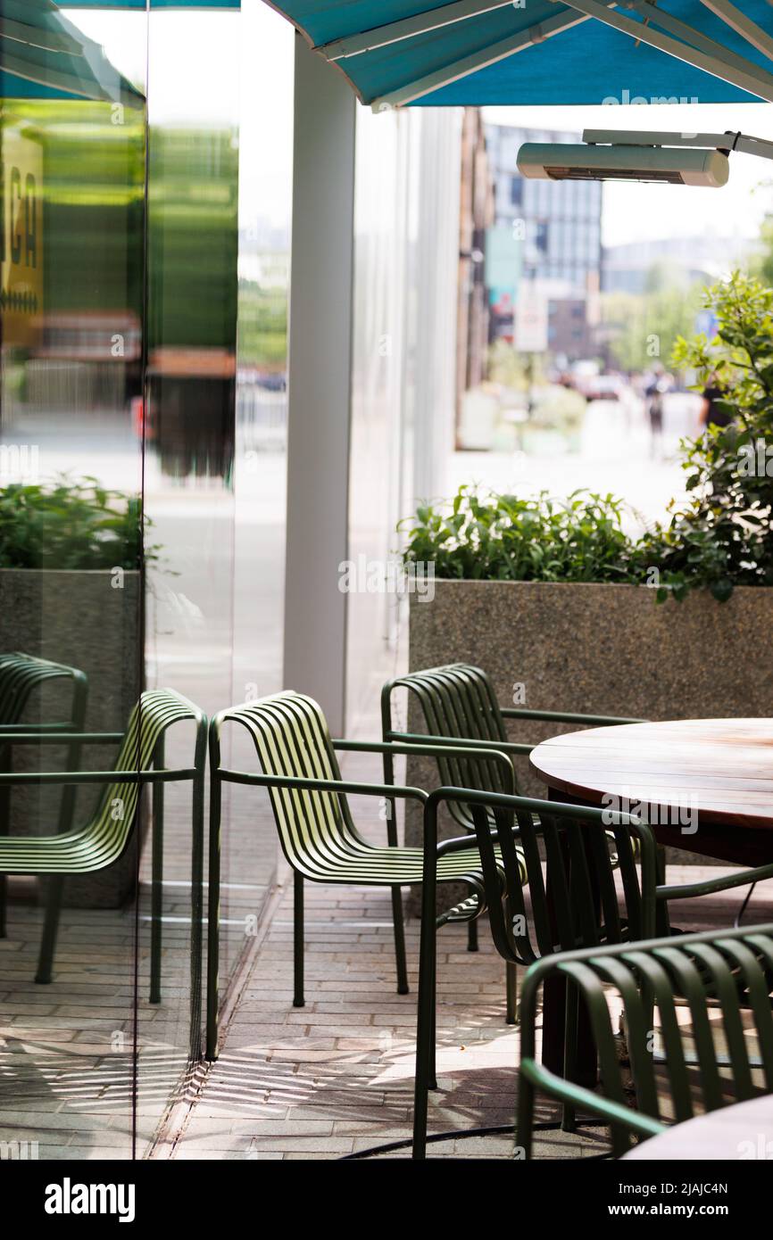 Grüne Stühle um einen Holztisch für Mahlzeiten im Freien in einem modernen Straßencafe/Restaurant Stockfoto