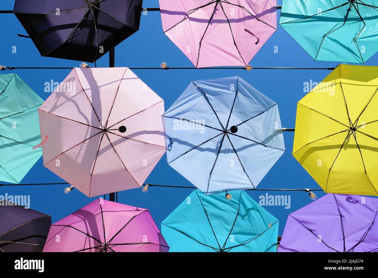 Regenschirme, die an Kabeln hängen, sorgen für einen Deckeneffekt; Reihen dekorativer, pastellfarbener Sonnenschirme, die im strahlend sonnendurchfluteten blauen Himmel durchscheinend sind Stockfoto