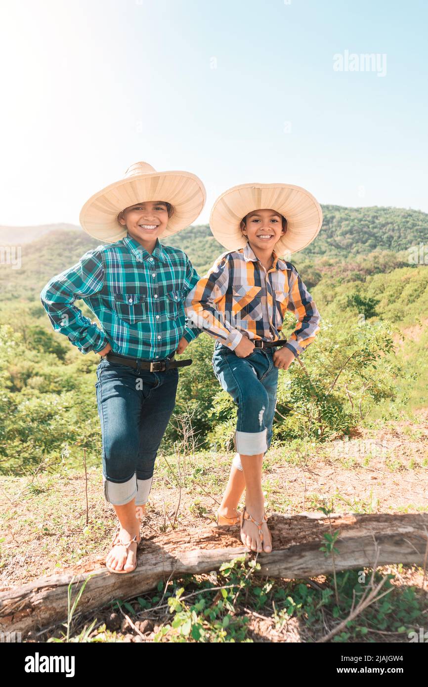 Vertikales Foto von zwei lateinischen Teenagern in traditioneller Landkleidung und Hüten, die lächeln, während sie auf einem Balken auf einem Berg stehen Stockfoto