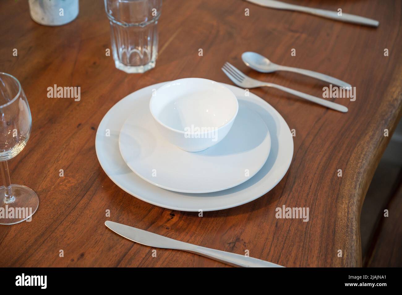 Ein Dinner-Restaurant mit weißen Tellern auf einem Holztisch. Ein Teller, ein Beilagenteller, eine Schüssel und ein Wasserglas. Stockfoto