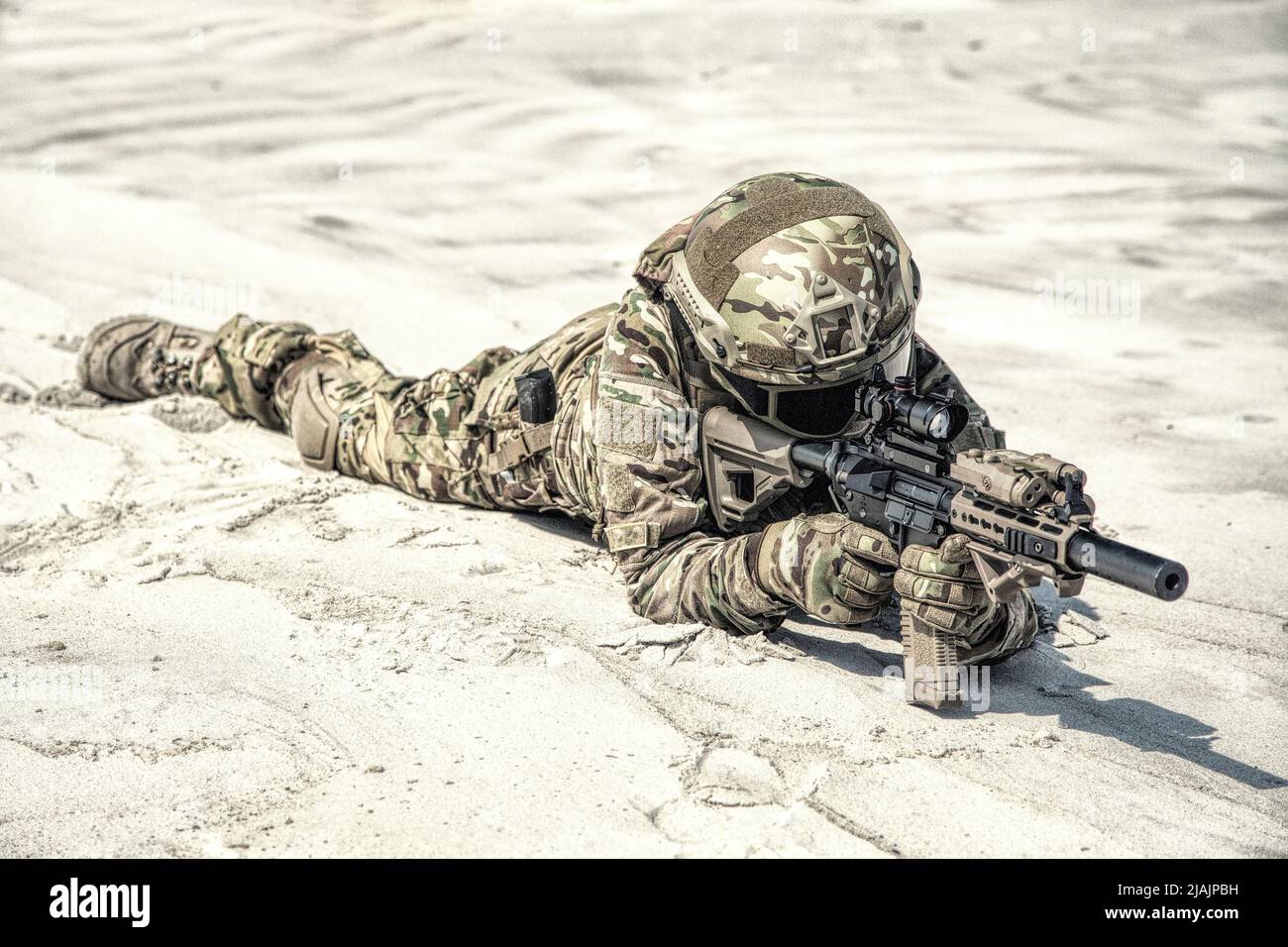 Militärangehöriger, der auf Sand liegt und ein Gewehr schießt, während er an der Simulation eines Wüstenschlagens teilnimmt. Stockfoto