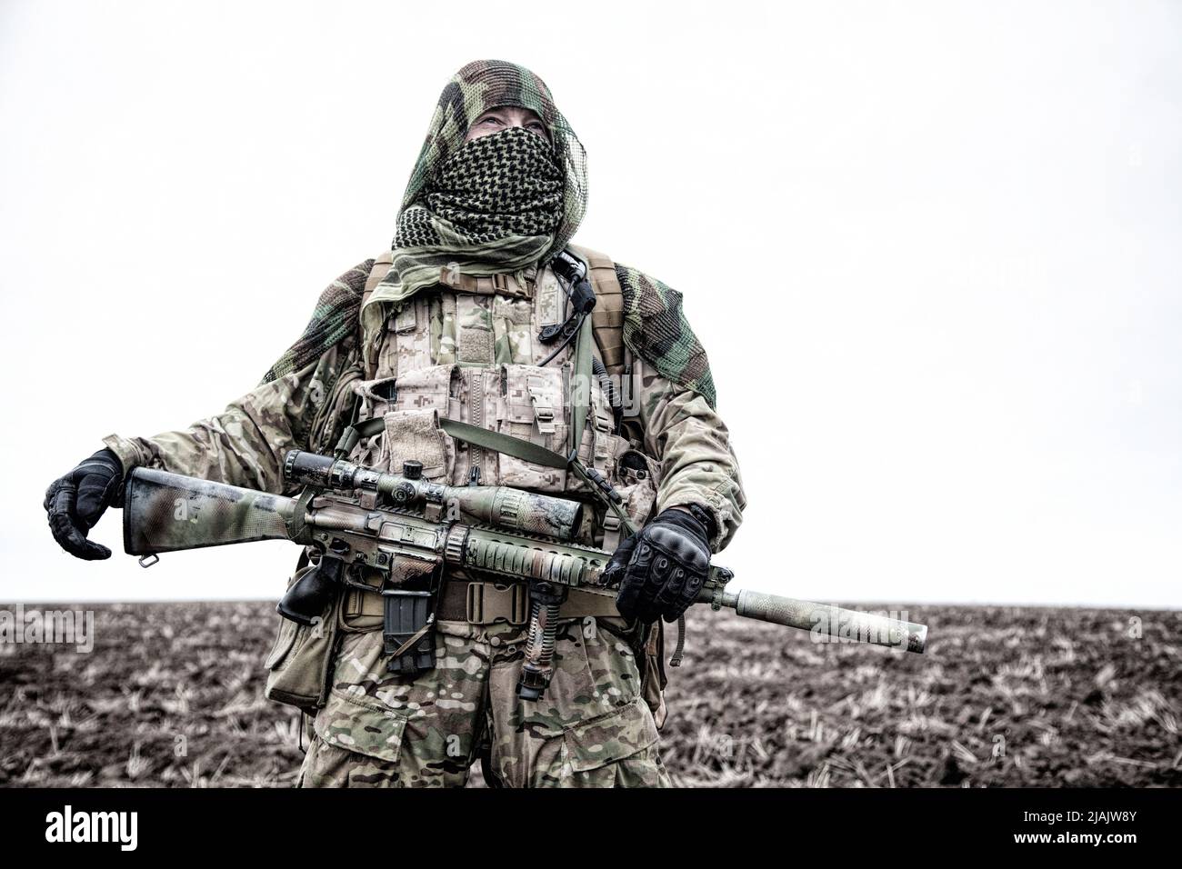 Armeesiper mit Gewehr auf dem Feld, Gesicht hinter shemagh versteckt. Stockfoto