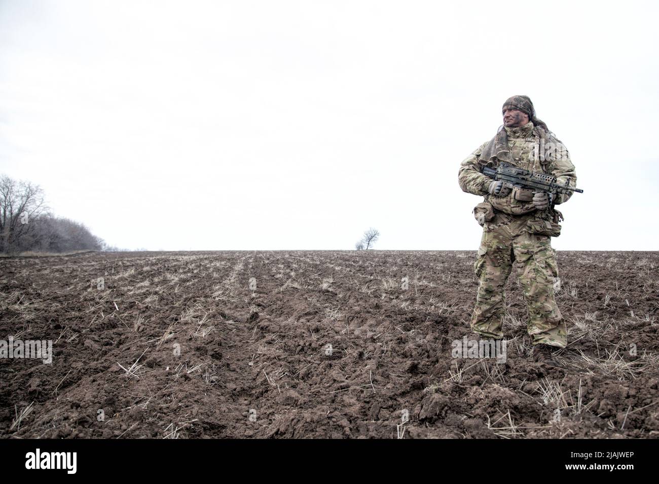 Soldat, der auf Patrouille mit Maschinengewehr auf einem schlammigen Feld steht. Stockfoto
