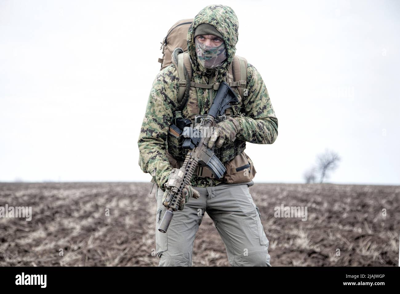 Militär Söldner tragen Kapuze Camo Jacke und Rucksack, zu Fuß durch schlammiges Gelände. Stockfoto