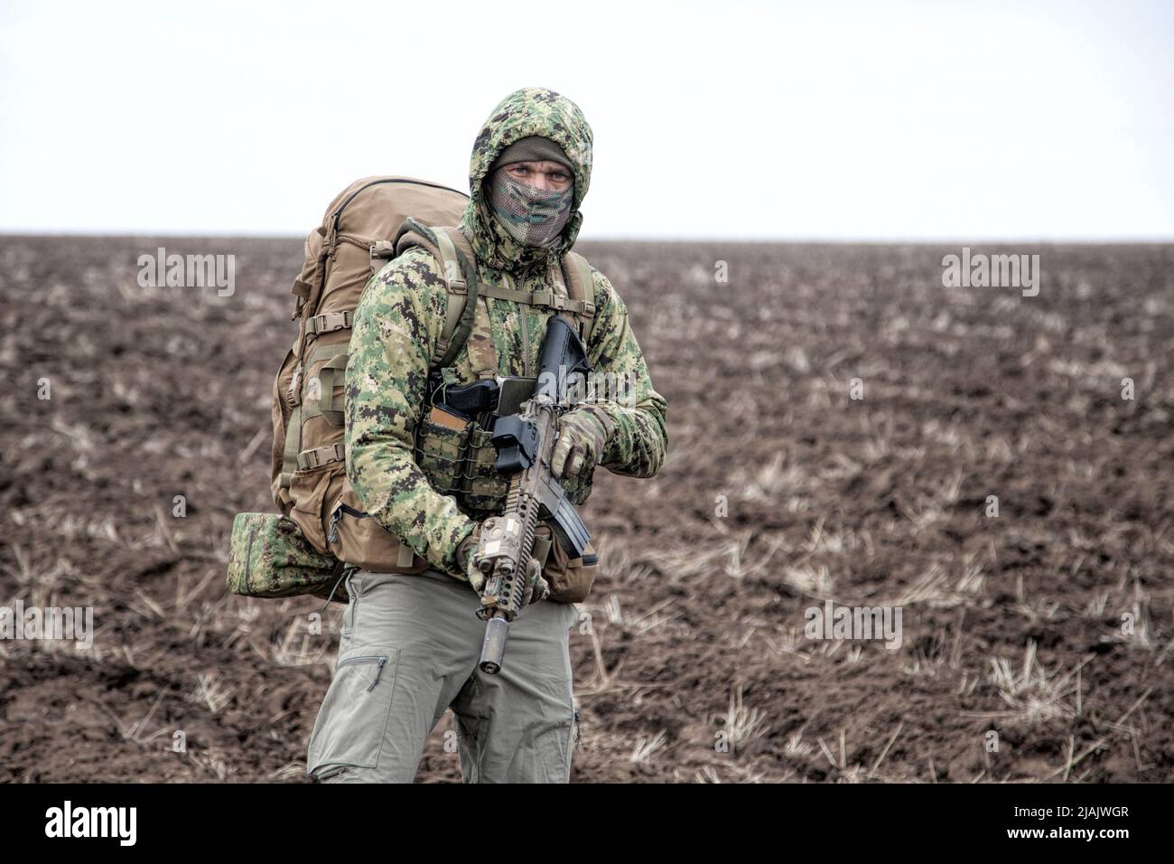 Militär Söldner tragen Kapuze Camo Jacke und Rucksack, zu Fuß durch schlammiges Gelände. Stockfoto