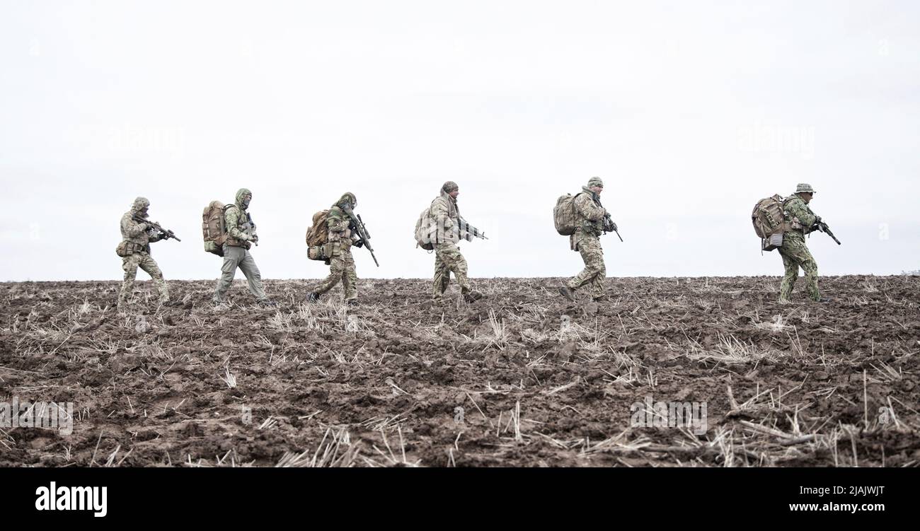Soldaten tragen Rucksäcke und gehen auf schlammigem Gelände. Stockfoto