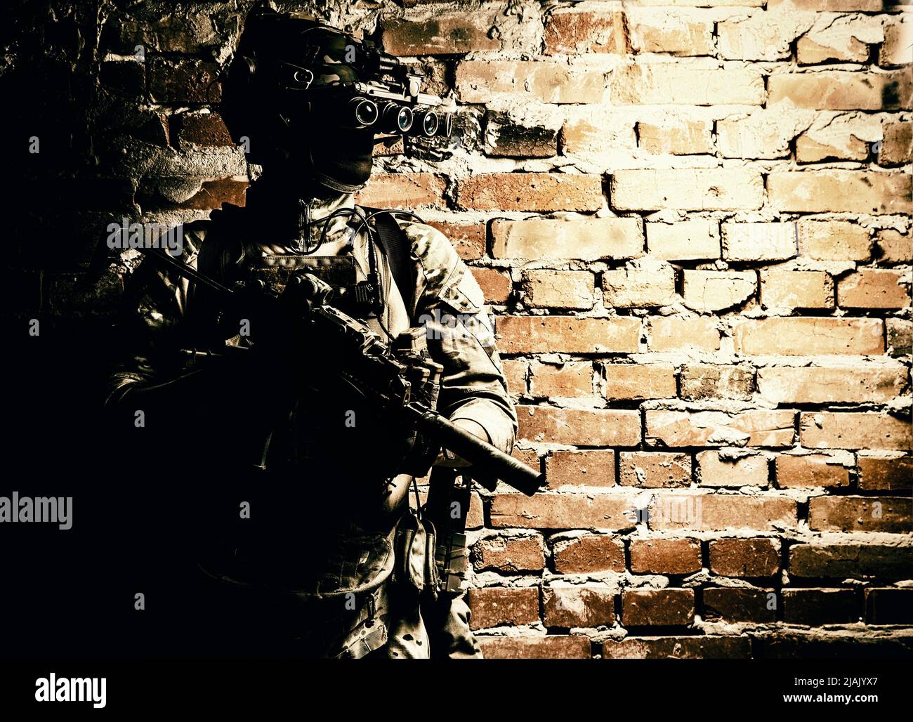 Special Forces Kämpfer, der gegen eine Ziegelwand steht, bewaffnet mit Wärmebildgerät auf Helm und Maschinengewehr. Stockfoto