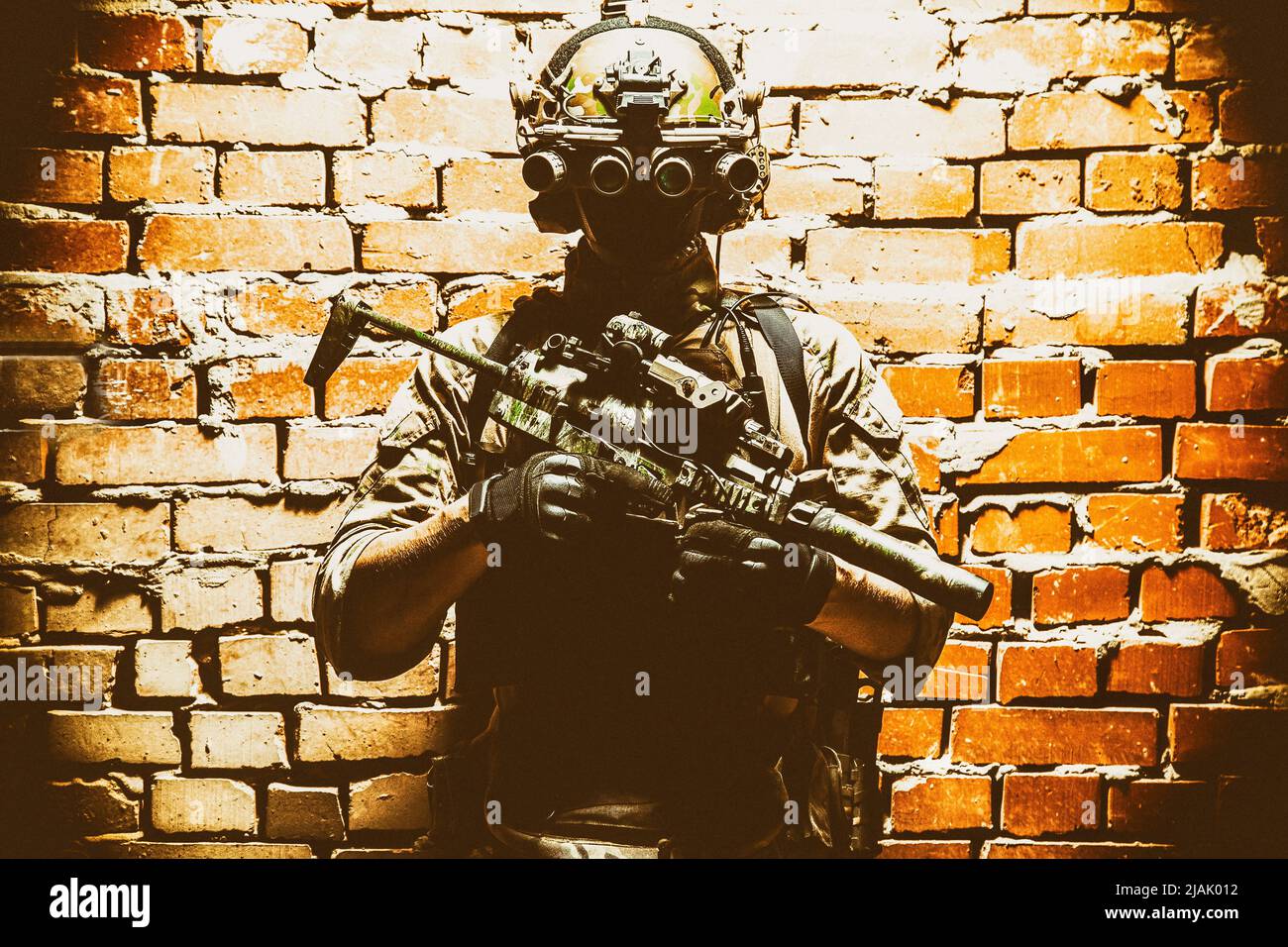 Special Forces Kämpfer, der gegen eine Ziegelwand steht, bewaffnet mit Wärmebildgerät auf Helm und Maschinengewehr. Stockfoto