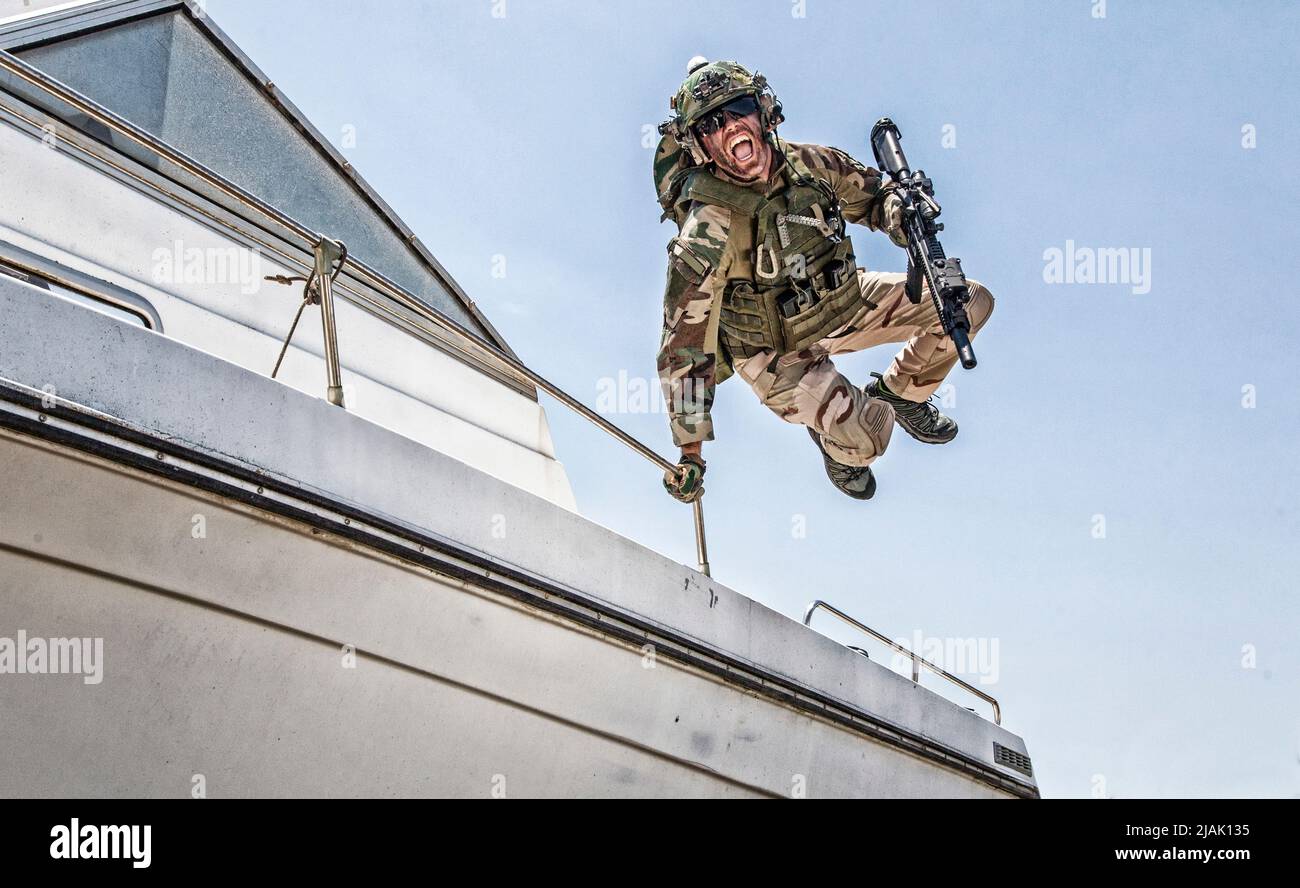 Der Soldat der Spezialeinheiten springt von einem Deck des Schnellbootes und landet mit einem Sturmgewehr an Land. Stockfoto