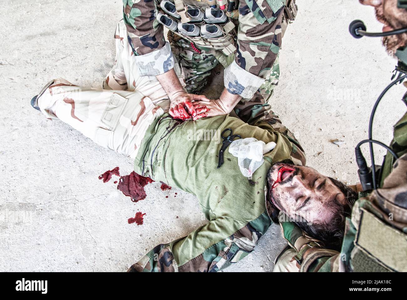 Soldaten, die einem verwundeten Kameraden, der auf dem Boden liegt, Nothilfe geben. Stockfoto