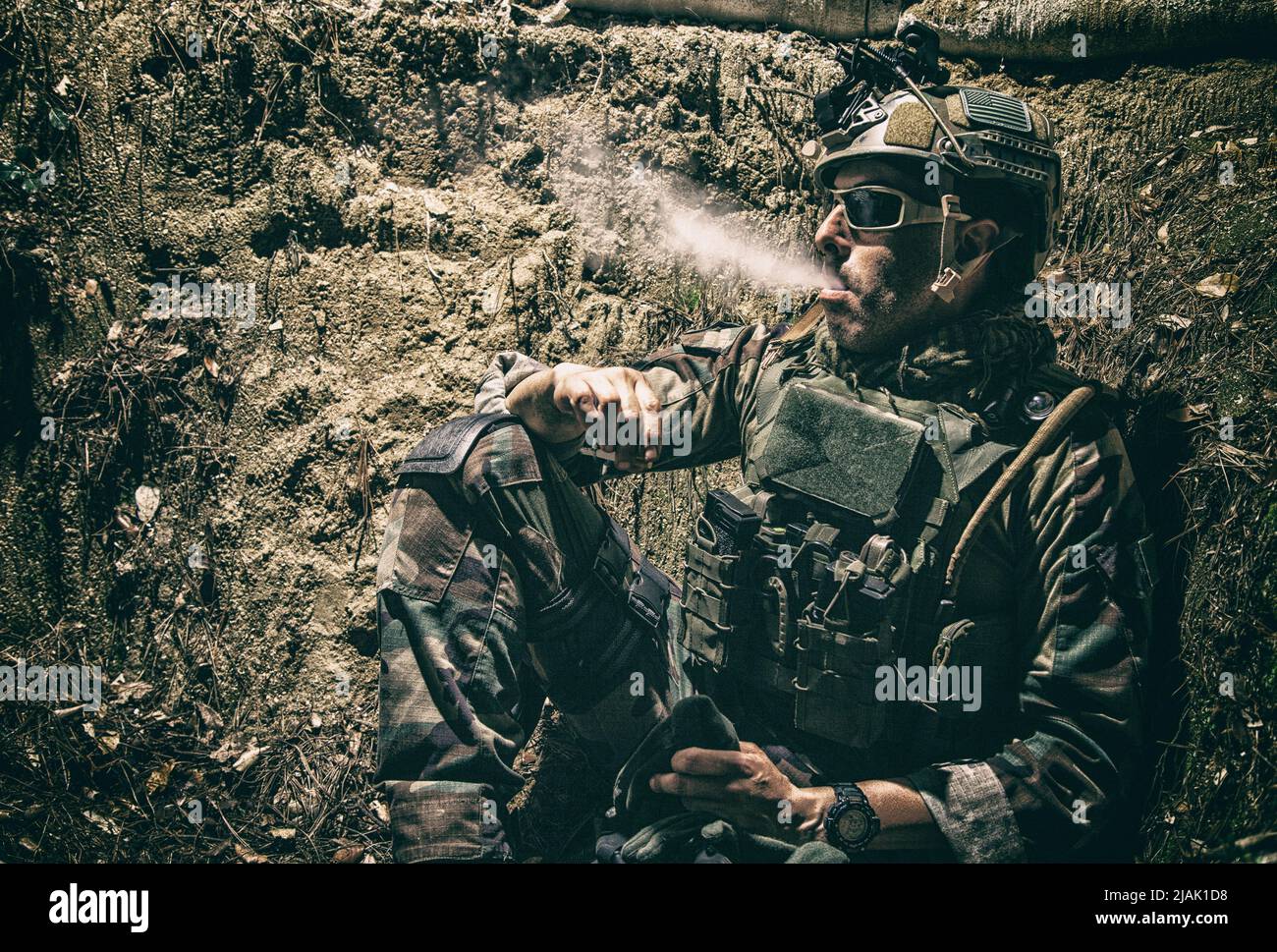 Ein Soldat, der nachts in den Schützengräben ruht und eine Zigarette raucht. Stockfoto