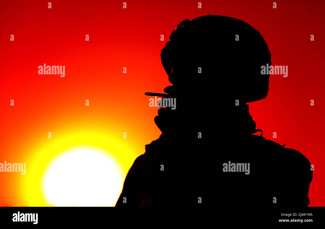 Silhouette eines Soldaten, der nachts vor einem roten Sonnenuntergang Zigarette raucht. Stockfoto