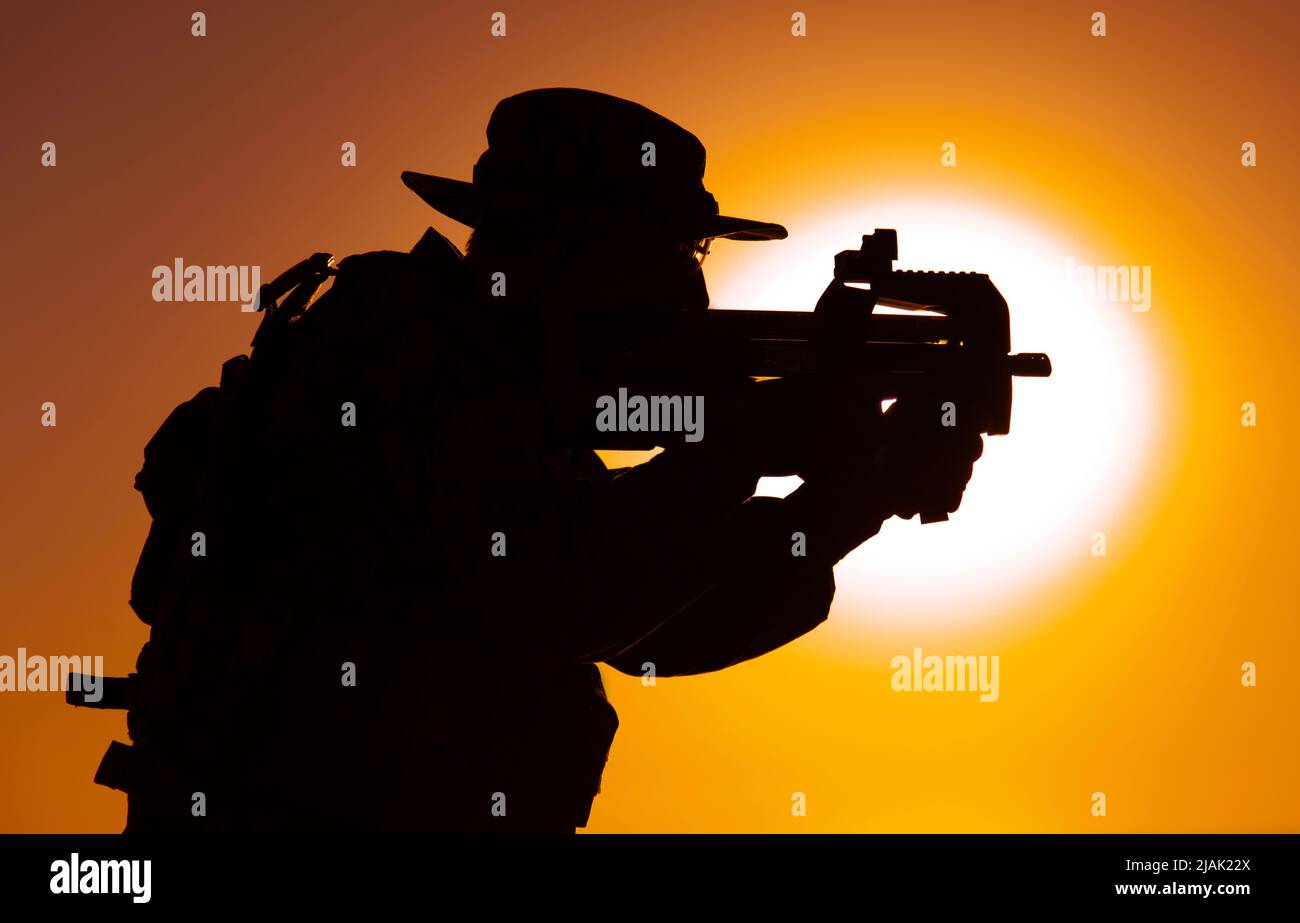 Silhouette eines Soldaten mit Bullpup Maschinengewehr auf dem Hintergrund der untergehenden Sonne. Stockfoto