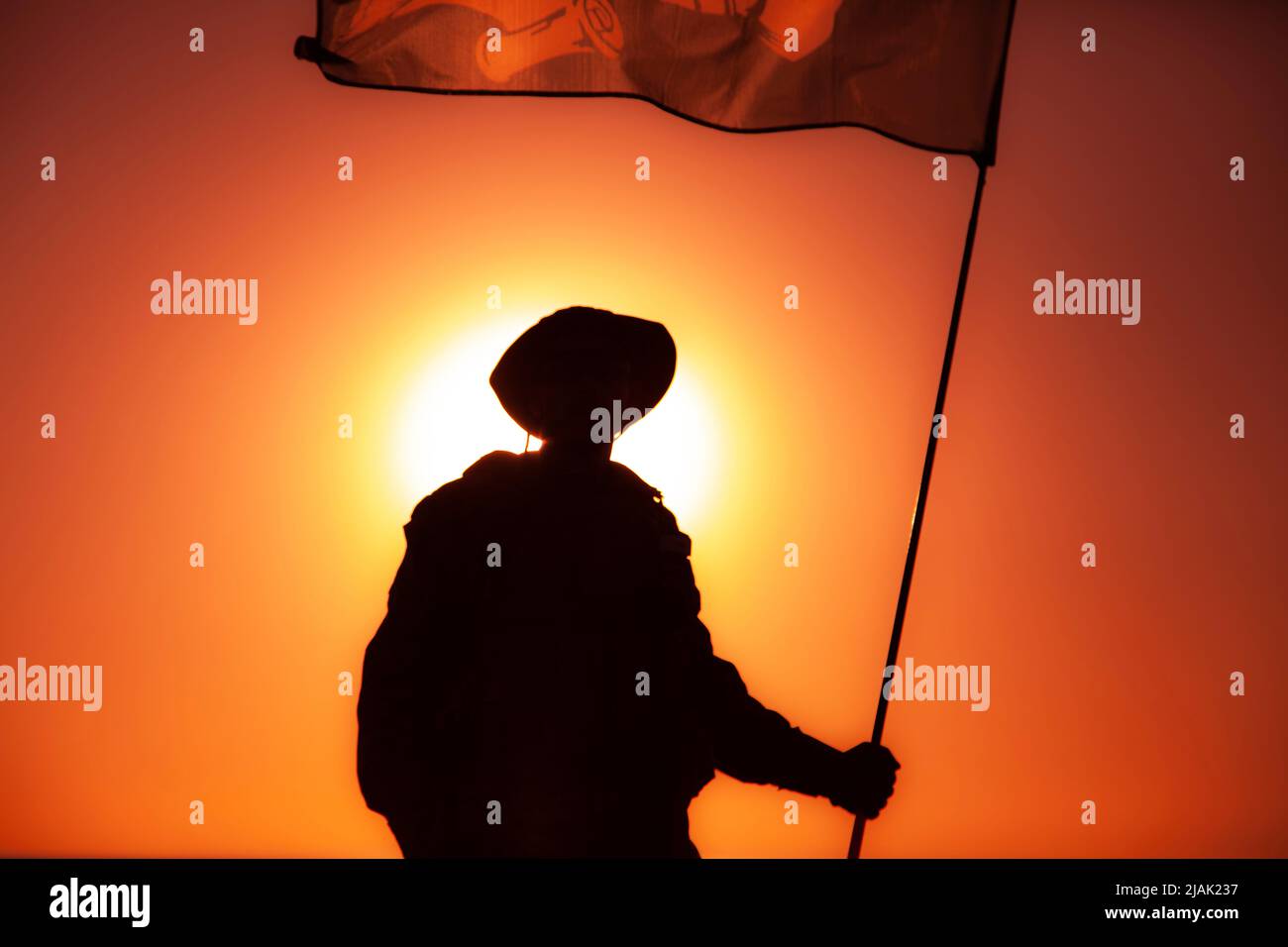 Silhouette eines Soldaten der Armee, der im Hintergrund eine Flagge gegen den Sonnenuntergang schwenkt. Stockfoto