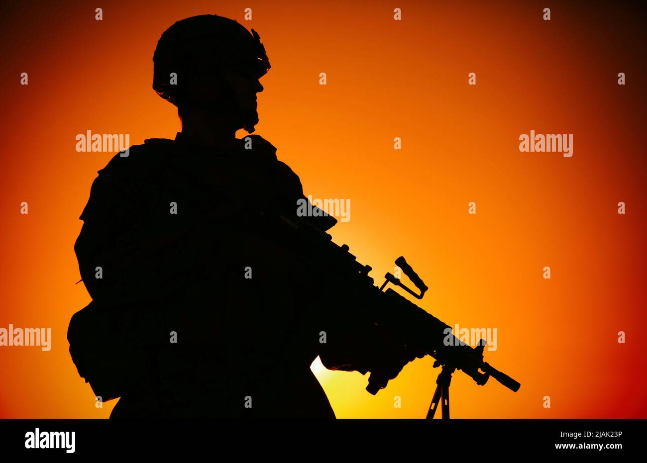 Silhouette eines Soldaten mit leichtem Maschinengewehr, der nachts gegen den Sonnenuntergang steht. Stockfoto