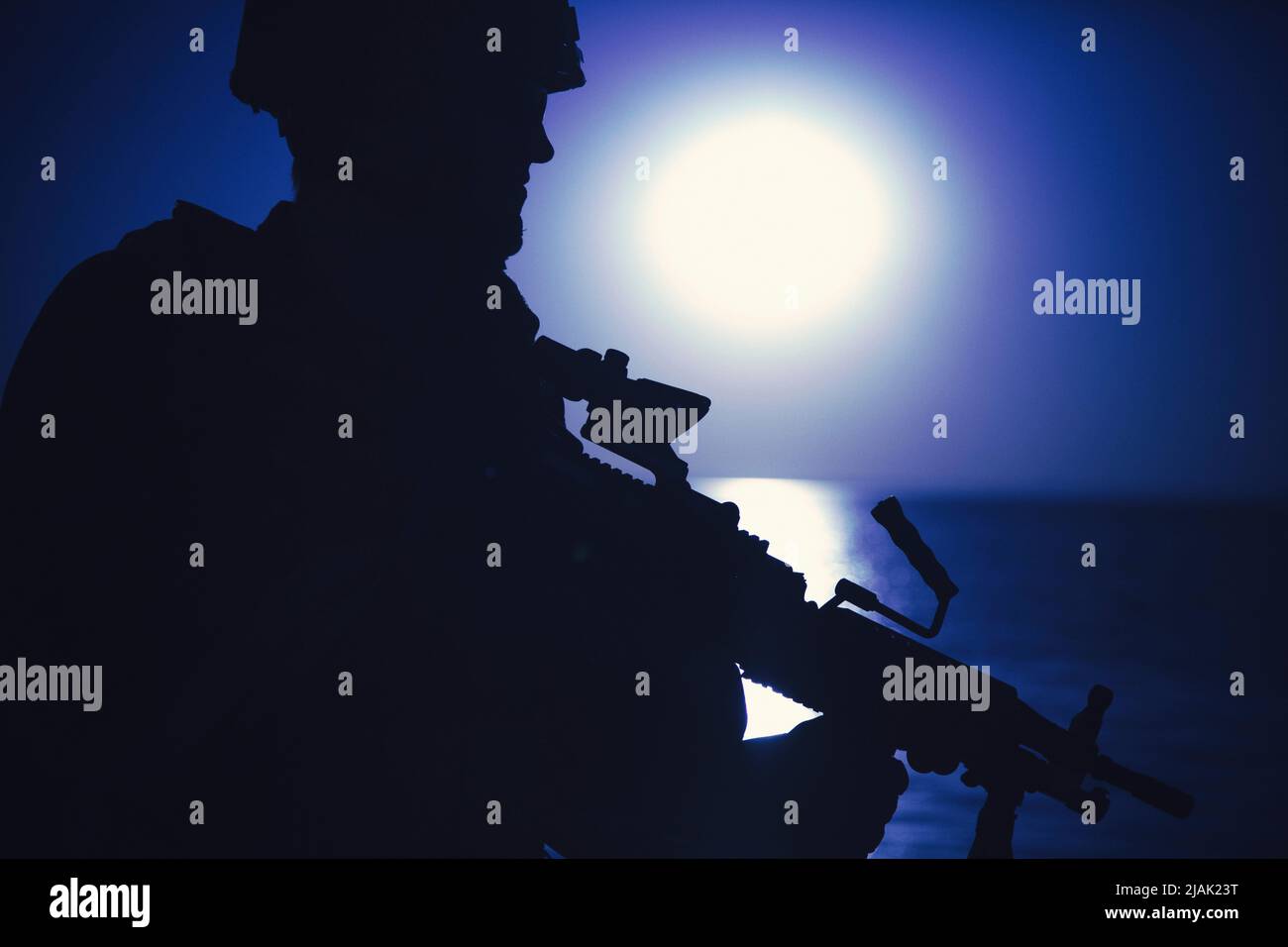Silhouette eines Soldaten auf patrouillierender Küste mit Maschinengewehr, gegen einen mondbeleuchteten Nachthimmel. Stockfoto