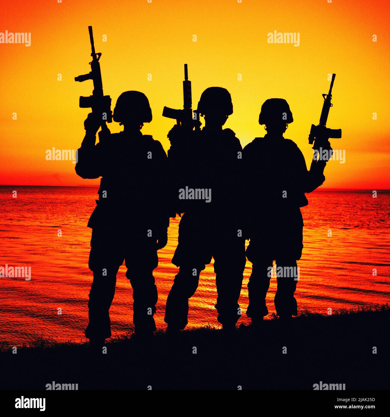 Silhouette einer Gruppe von Soldaten, die bei Sonnenuntergang am Ufer stehen und Sturmgewehre hochgezogen haben. Stockfoto