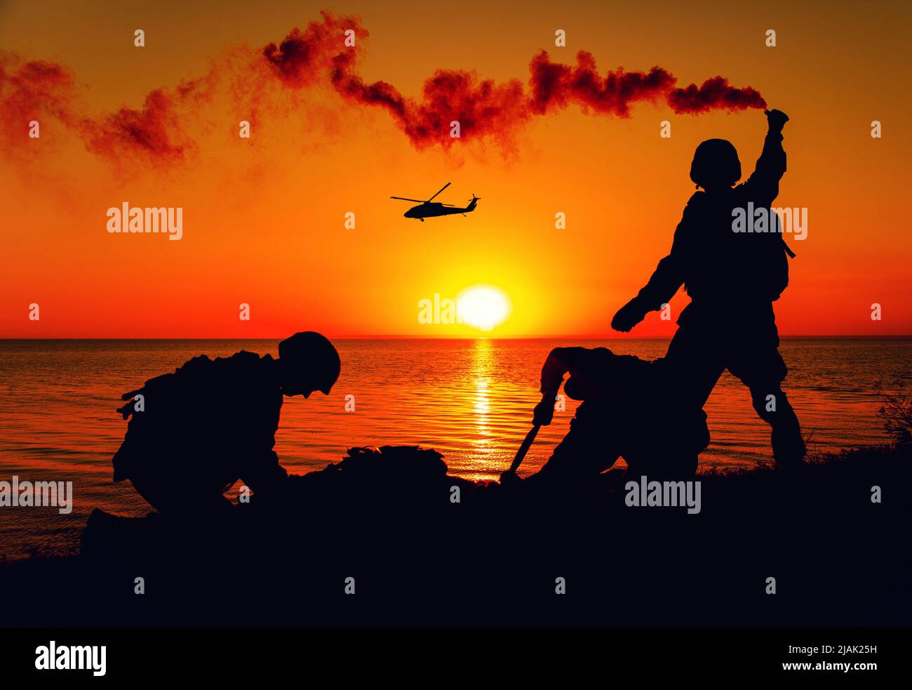 Silhouette von Soldaten, die einem Hubschrauber mit Rauchflackern signalisieren, während sie auf die Evakuierung am Ufer warten. Stockfoto