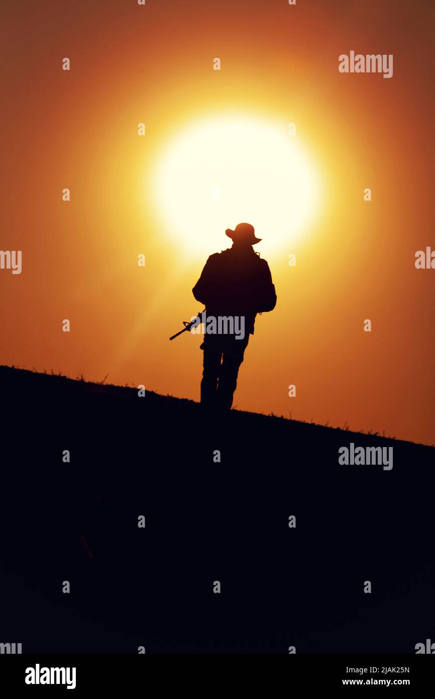 Silhouette eines Soldaten, der bei Sonnenuntergang auf einem Gebiet patrouilliert. Stockfoto