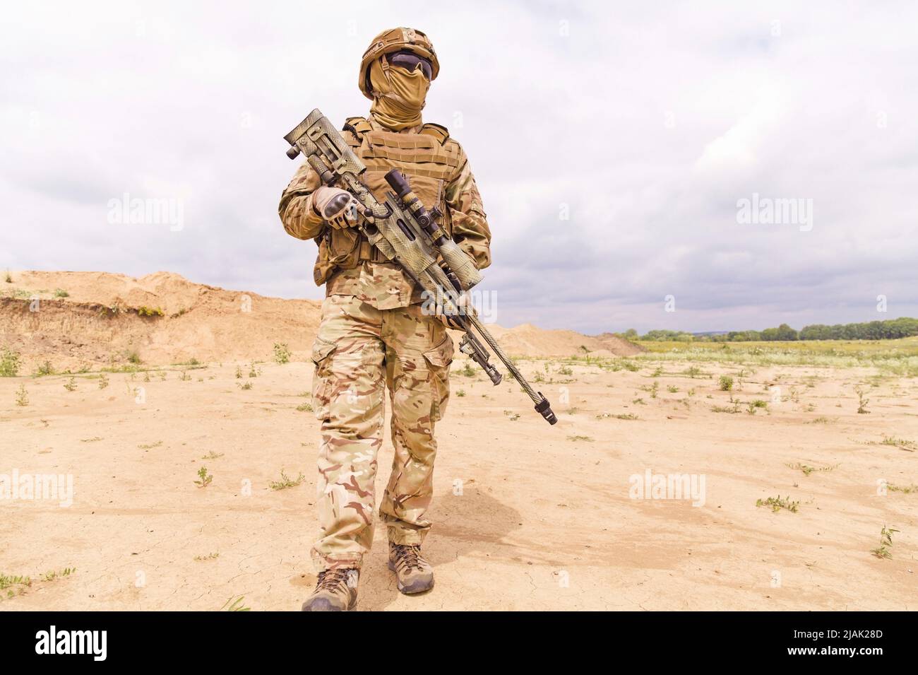 Bewaffneter und bewaffneter Soldat der Spezialeinheiten mit Scharfschützengewehr, der in der Wüste steht. Stockfoto