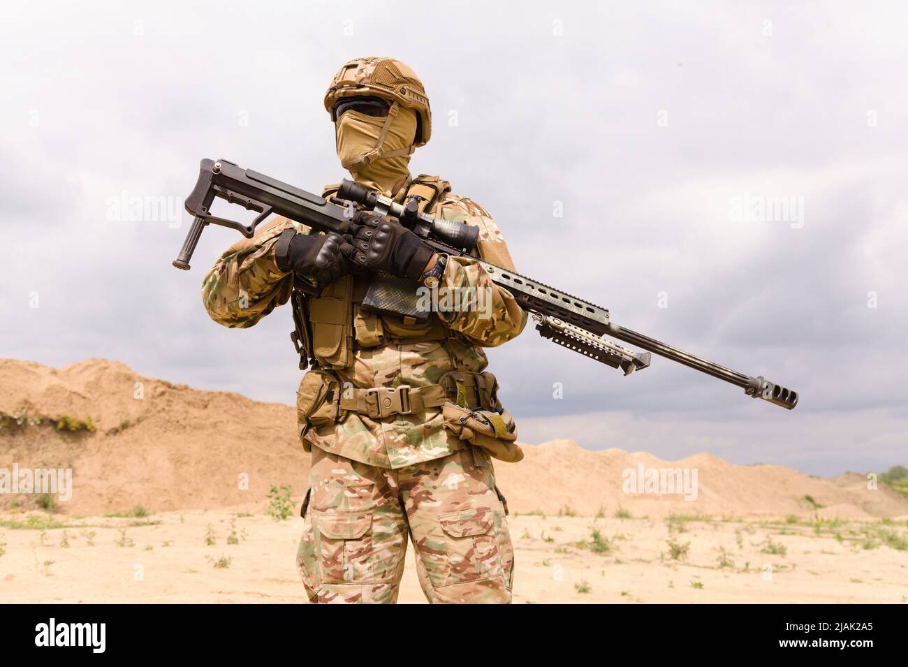 Soldat in Tarnung hält Scharfschützengewehr, während er in der Wüste steht. Stockfoto