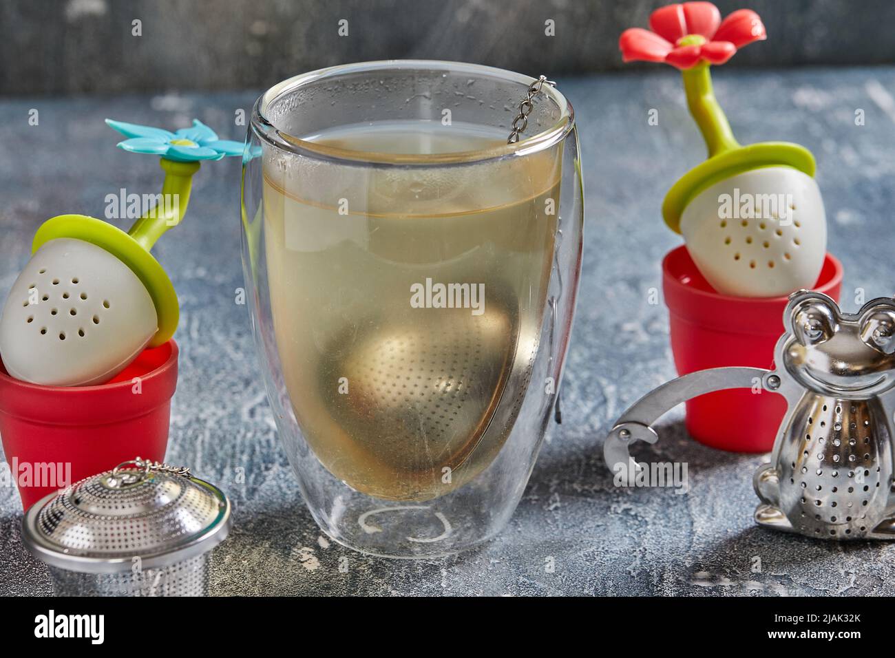 Tee-Brauwerkzeuge in Form von Fröschen und Blumen mit einem Glas Tee Stockfoto