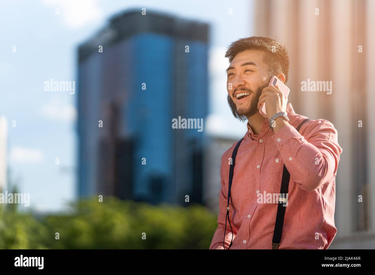 Lächelnder asiatischer Geschäftsmann im Gespräch mit dem Handy im Freien Stockfoto