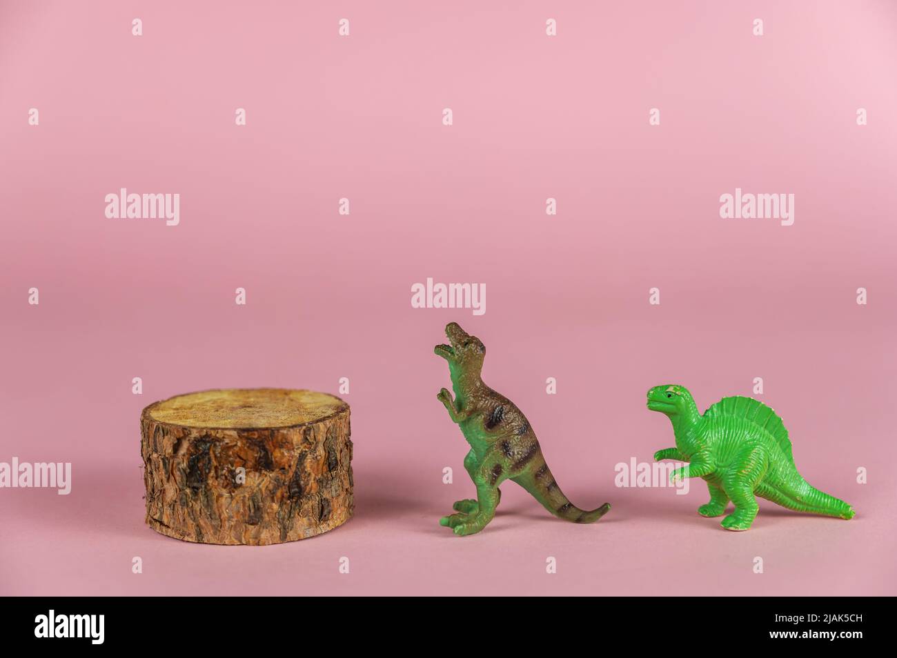 Die Dinosaurier-Miniaturen stehen neben dem Kiefernsockel vor dem rosa Hintergrund. Kleine grüne Figuren von räuberischen Dinosauriern stehen auf ihrer Hinterhand Stockfoto