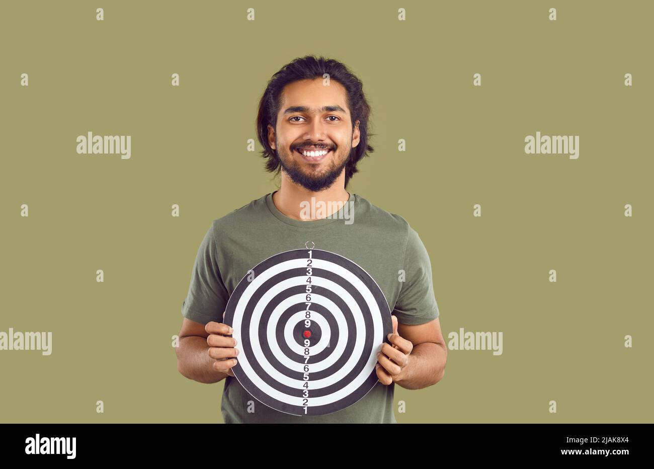 Glücklich lächelnder indischer Kerl hält Schießziel, um Konzept der Festlegung von Zielen zu zeigen Stockfoto