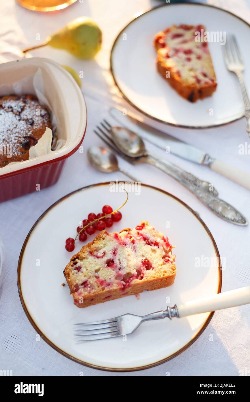 Garten und Stillleben. Teeparty im Garten - ein Stück Johannisbeerkuchen auf einem Teller auf einem Tisch mit einer weißen Tischdecke Stockfoto