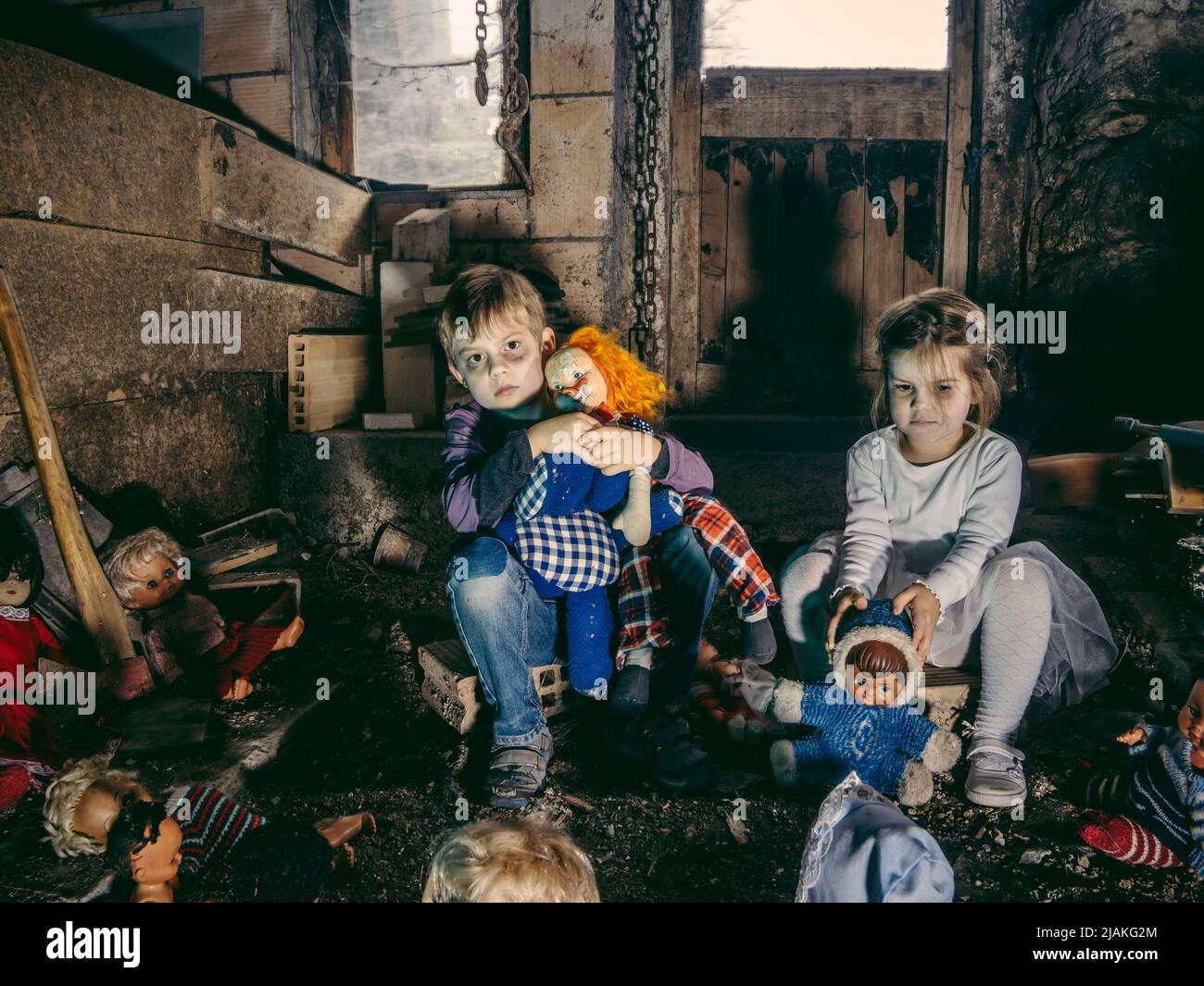 Gruselige kleine Kinder, die mit alten Puppen in einer Scheune sitzen, die mit Spinnweben und Staub bedeckt ist. Stockfoto