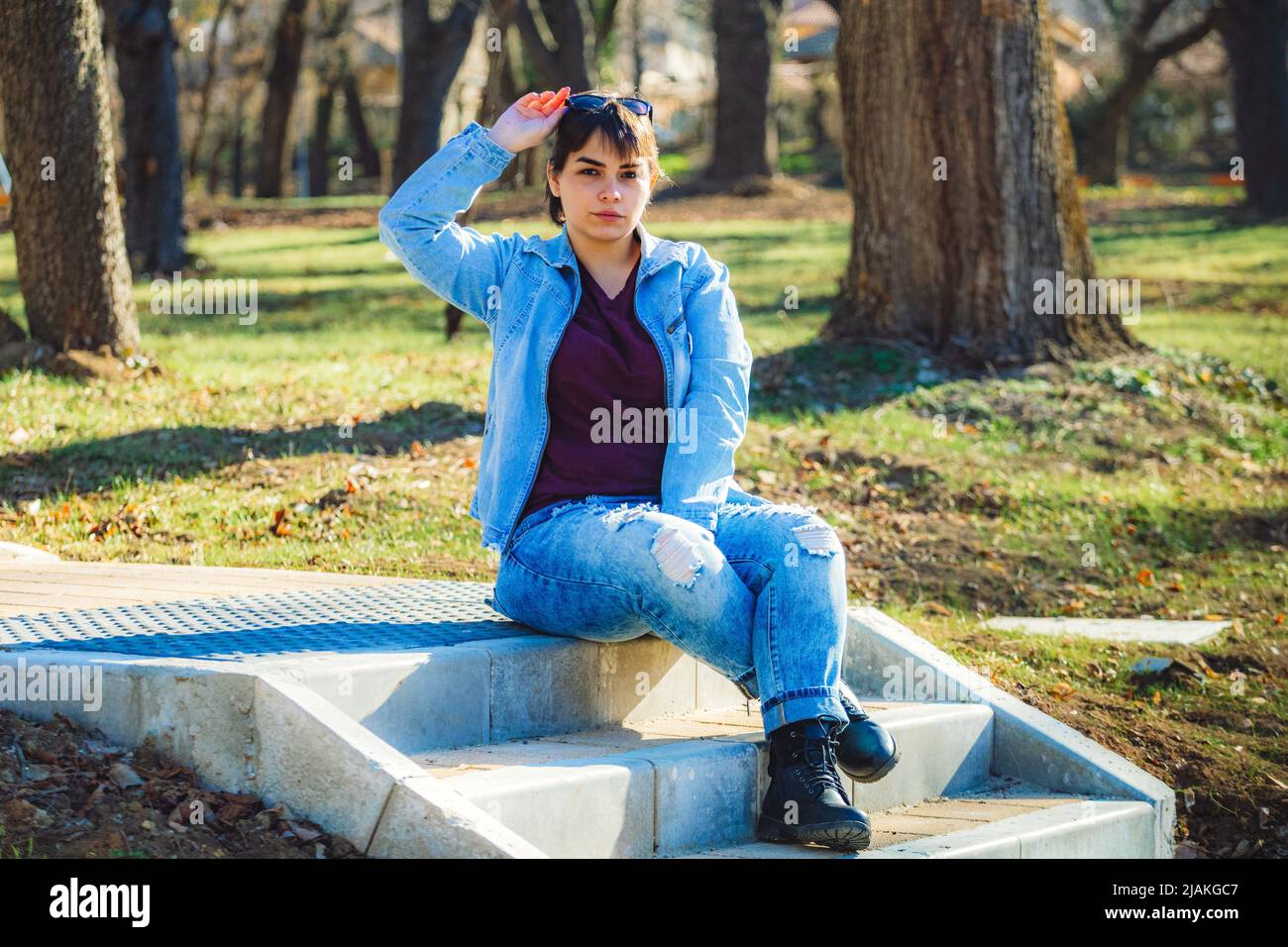 Schönes Mädchen mit kurzen schwarzen Haaren in ihrem 20s im Park trägt hellblaue Jeans und eine hellblaue Denim-Jacke Stockfoto