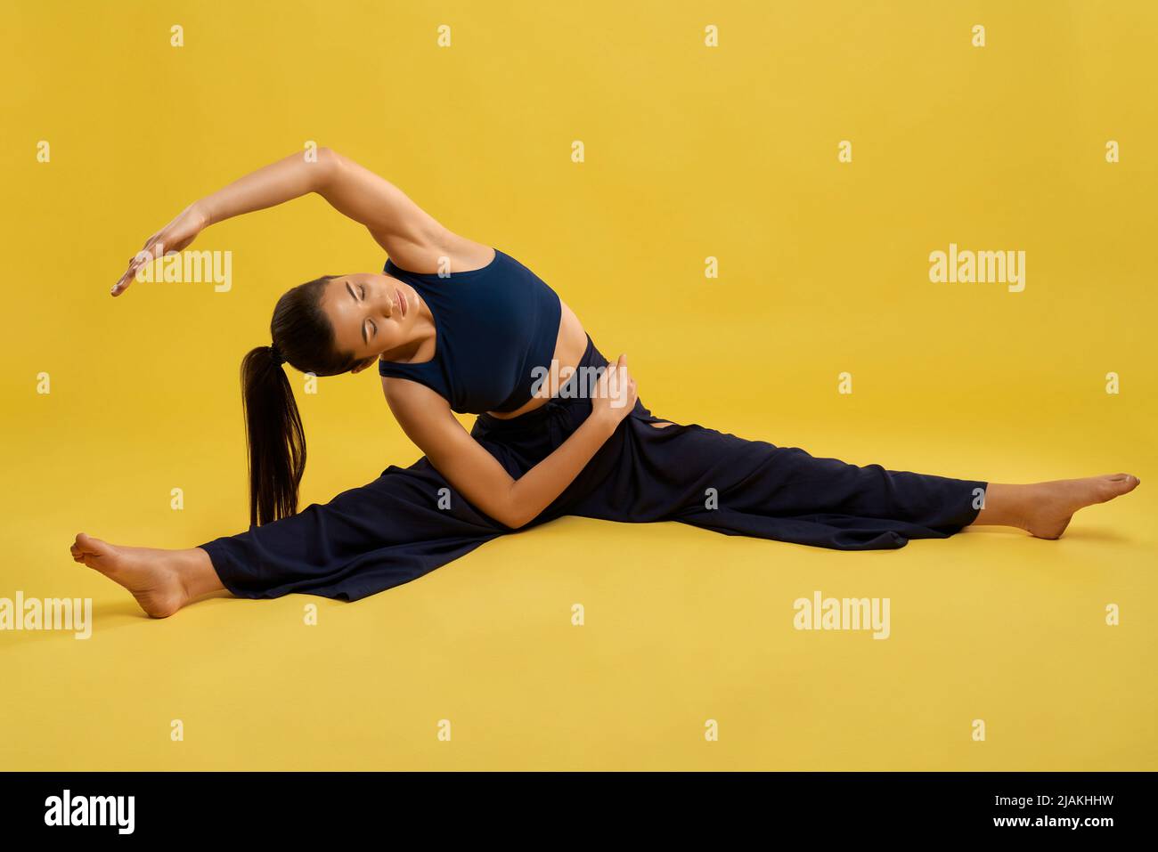 Hübsche Frau, die Yoga-Asana praktiziert, die Beine dehnt und sich drinnen zur Seite lehnt. Barfuß Mädchen mit geschlossenen Augen versuchen, Hand zu Fuß zu erreichen, während Yoga, isoliert. Konzept der Ausübung. Stockfoto
