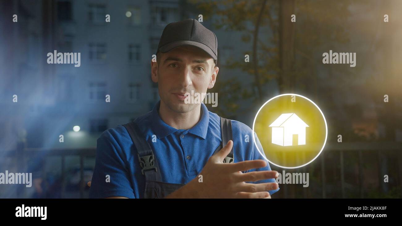Glücklicher junger Lieferkurier in blauer Kappe, der das Heimsymbol mit der Hand zeigt. Versandkonzept Stockfoto