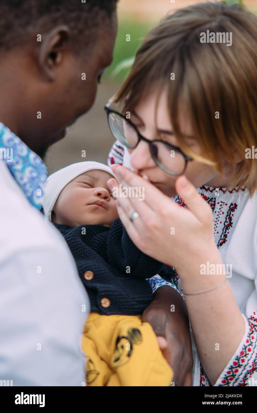 Happy interracial Familie in ukrainischen nationalen bestickten Shirts gekleidet hält und küsst Hand ihres neugeborenen Babys. Konzept der interracial Familie A Stockfoto